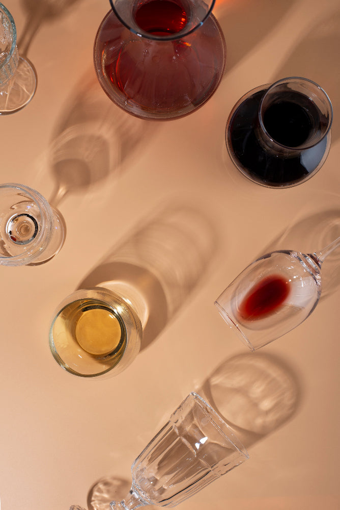 Elegant still life composition of wine glasses and a decanter casting soft shadows on a warm-toned surface, featuring red, white, and sparkling wines.