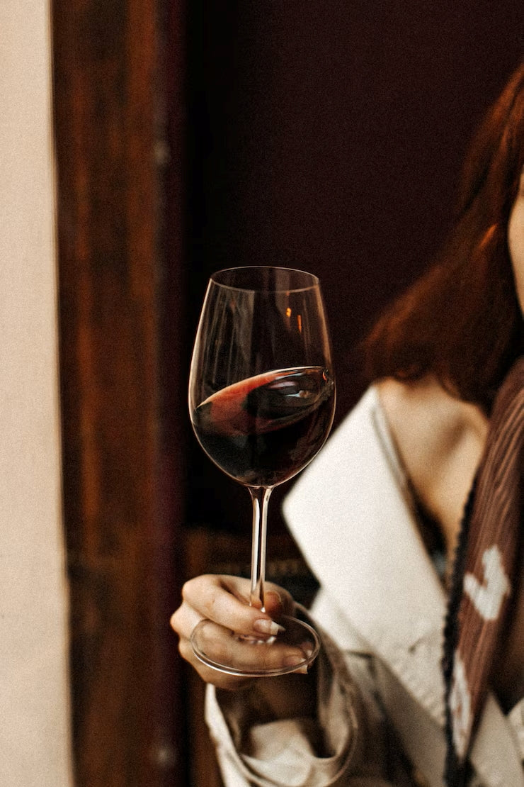 Elegant woman holding a glass of red wine in a dimly lit setting, evoking a sense of luxury and sophistication.