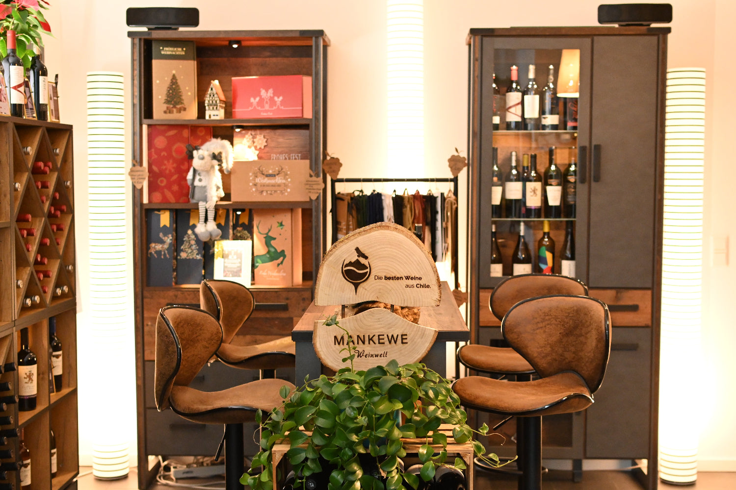 Cozy and elegant interior of the Mankewe Weinwelt store, featuring wine shelves, decorative lighting, seating, and a wooden sign with the brand logo.